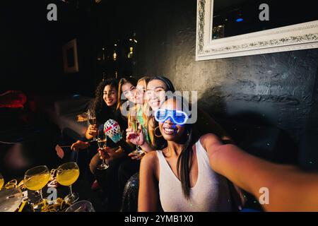 Eine Gruppe junger Frauen macht ein Selfie, während sie einen lebhaften Abend mit Getränken und Lachen genießen und unvergessliche Momente zusammen in einem festlichen fest festhalten Stockfoto