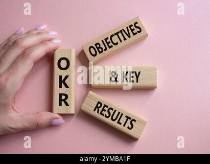 Symbol für OKR-Ziele und wichtige Ergebnisse. Holzblöcke mit den Worten OKR-Ziele und wichtige Ergebnisse. Geschäftsmann Hand. Schöner rosafarbener Hintergrund. Unternehmen Stockfoto