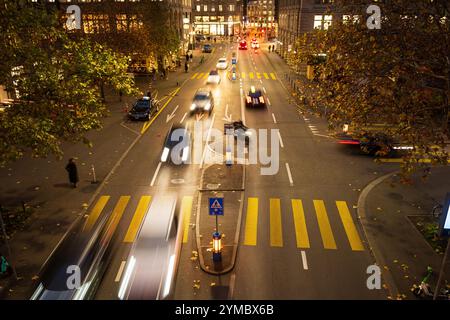 Autoverkehr auf belebter Straße mit Fußgängerüberquerung nachts in einer Stadt in Europa. Über der Sicht, verschwommene Autos und Menschen. Stockfoto