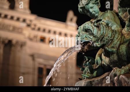Alter, verwitterter, bronzener Wasserbrunnen-Statuenkopf mit Wasser, das aus dem Mund strömt. Nahaufnahme, Nachtaufnahme, geringe Schärfentiefe, keine Leute Stockfoto