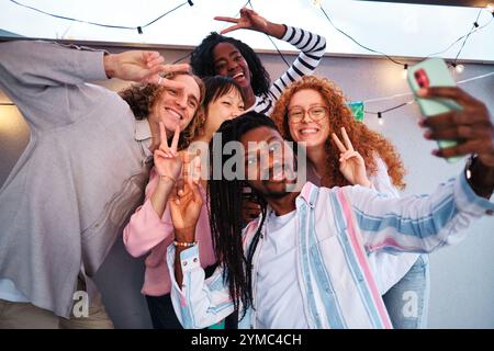 Glückliche multiethnische Freunde machen ein Selfie und machen Siegeszeichen auf der Dachparty Stockfoto
