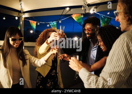 Multiethnische Freunde, die bei einer Dachparty mit Champagner anstoßen Stockfoto