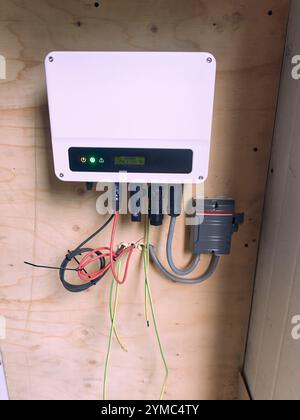 Kleiner Solar-Wechselrichter für Wohnzwecke, der im niederländischen Haus auf einer Holzplatte installiert wird, komplett mit Wartungsschalter und Erdung. Stockfoto