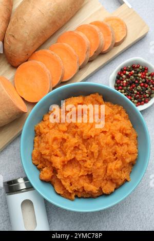 Leckere Süßkartoffelpüree in der Schüssel, frisches Gemüse und Gewürze auf grauem Tisch, flache Ladefläche Stockfoto