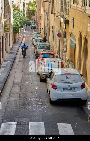 Marseille. Frankreich - 21. November 2024: Eine enge Straße in Marseille mit geparkten Autos auf beiden Seiten und einem Motorradfahrer, der gegen den Verkehr fährt. Die Stre Stockfoto