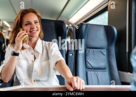 Junge Geschäftsfrau, die auf ihrem Smartphone spricht, während sie geschäftlich mit dem Zug unterwegs ist. Stockfoto