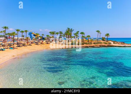 Ayia Napa, Zypern, mit goldenen Sandstränden und türkisfarbenem Wasser, Palmen und Sonnenliegen schaffen ein tropisches Paradies. Perfekt zum Entspannen, mit Stockfoto