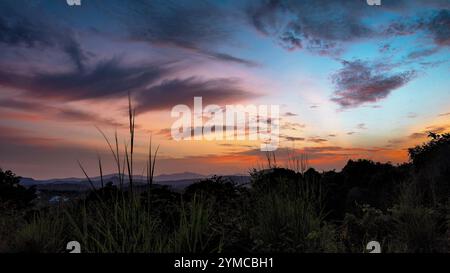 Ein atemberaubender Sonnenuntergang färbt den Himmel in leuchtenden Orange-, Rosa- und Violetttönen und strahlt einen warmen Glanz über den fernen Hügeln aus. Stockfoto