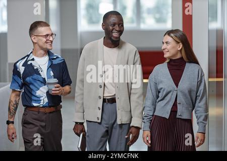 Mittelgroße Aufnahme positiver männlicher afroamerikanischer Boss in eleganter Freizeitkleidung, der mit Mitarbeitern Gespräche führt, während er geschäftlich unterwegs ist Stockfoto