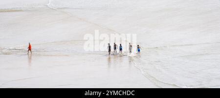 Ein Panoramabild eines RNLI-Rettungsschwimmers, der vor einer Gruppe von Urlaubern am Crantock Beach in Newquay in Cornwall in Großbritannien, Europa, spaziert. Stockfoto