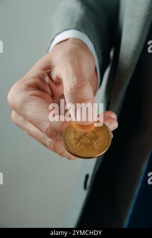 Nahaufnahme eines Geschäftsmannes, der einen eleganten grauen Anzug trägt und drinnen einen Bitcoin in der Hand hält Stockfoto