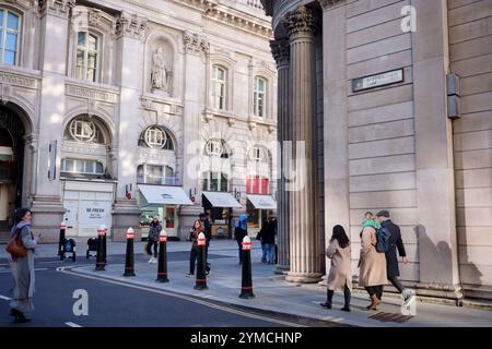 Stadtarbeiter laufen am 20. November 2024 in London, dem Finanzviertel der Hauptstadt, über die Ecke Threadneedle Street und Batholomew Lane, unter der Architektur der Bank of England (rechts). Stockfoto