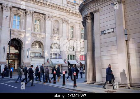 Stadtarbeiter laufen am 20. November 2024 in London, dem Finanzviertel der Hauptstadt, über die Ecke Threadneedle Street und Batholomew Lane, unter der Architektur der Bank of England (rechts). Stockfoto