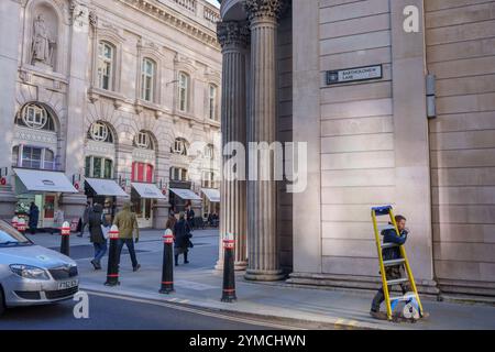 Stadtarbeiter laufen am 20. November 2024 in London, dem Finanzviertel der Hauptstadt, über die Ecke Threadneedle Street und Batholomew Lane, unter der Architektur der Bank of England (rechts). Stockfoto