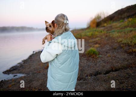 Rückansicht einer Frau, die Yorkshire Terrier am Seeufer hält Stockfoto