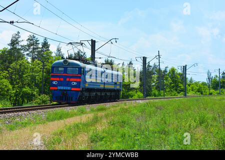 Transport, Schienentransport, Maschinen. Ein alter, in Betrieb befindlicher blauer Metallzug fährt entlang breiter Metallbahnlinien. Stockfoto