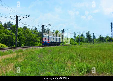 Transport, Schienentransport, Maschinen. Ein alter, in Betrieb befindlicher blauer Metallzug fährt entlang breiter Metallbahnlinien. Stockfoto