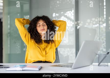 Die junge Frau macht eine entspannende Pause am Schreibtisch mit Laptop und genießt einen Moment der Ruhe. Konzept der Arbeitsplatzentspannung, psychischen Gesundheit am Arbeitsplatz und Stressabbau. Stockfoto