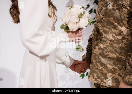 Emotionale Hochzeitszeremonie zwischen einer Braut in weißem Kleid und einem Soldaten in Camouflage-Uniform. Stockfoto