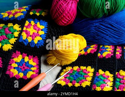 Farbenfrohe Baumwoll-Oma-Quadrat. Häkeln Sie die Textur in Nahaufnahme, Haken und Fadenkugeln. Stockfoto