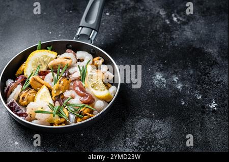 Roher Mix aus Meeresfrüchten mit Garnelen, Garnelen, Muscheln, Tintenfisch und Tintenfisch in einer Pfanne, die zum Kochen bereit ist. Schwarzer Hintergrund. Draufsicht. Speicherplatz kopieren. Stockfoto