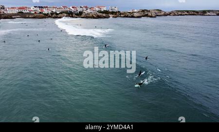 Surfer im Wasser und auf ihren Surfbrettern warten auf ihre nächste Welle an einem Strand in Portugal Stockfoto