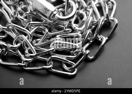 Metallkette mit Befestigungsschelle in ordentlichem Haufen. Glatte, polierte Verbindungsglieder und ein sicherer Clip sorgen für ein funktionelles und dennoch dekoratives Element auf Schwarz Stockfoto