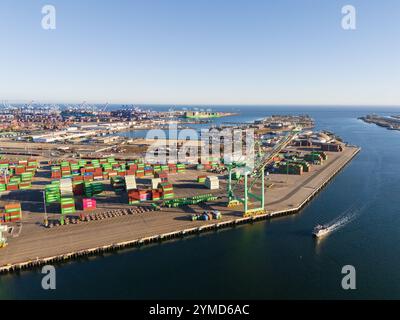 Hohe Luftaufnahme von Frachtcontainer-Terminals, Schiffskranen und einem Boot, das den Kanal im Hafen von Long Beach, Kalifornien, durchquert Stockfoto