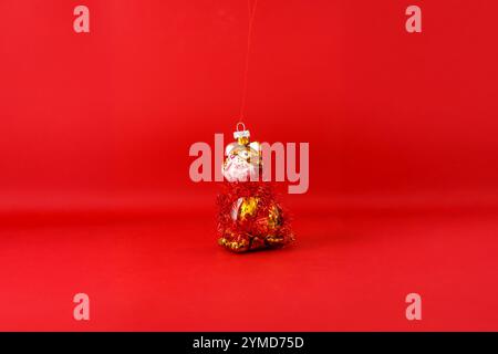 Ein Weihnachtsschmuck in Form einer Katze. Eine rote Lametta-Girlande um ihren Körper gewickelt. Überwiegend Gold und weiß mit detaillierten Details, der bac Stockfoto