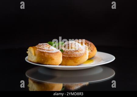 Backwaren. Süßbrötchen mit Hüttenkäsefüllung und Honig auf einem Teller isoliert auf schwarzem Hintergrund. Stockfoto