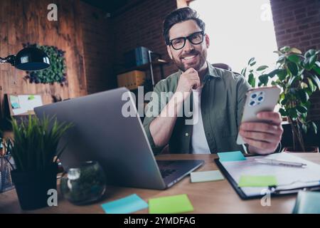 Foto von hübschem jungen Mann interessierter Manager halten Gerät Netbook gekleidetes grünes Hemd komfortables Startup Büro Loft Raum Innenraum Stockfoto