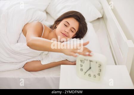 Junge Frau schlafend aufwachen lächelnd morgens in bequemem, weichem Bett liegend, Alarm ausschalten Stockfoto
