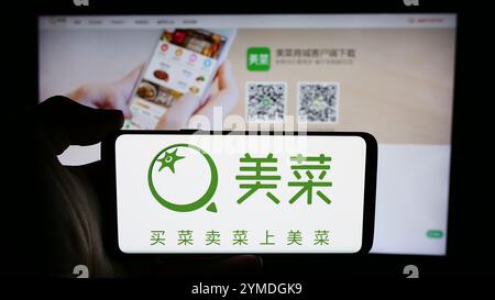 In dieser Fotoabbildung hält eine Person ein Smartphone mit dem Logo des chinesischen landwirtschaftlichen E-Commerce-Unternehmens Meicai vor der Business-Website. Stockfoto