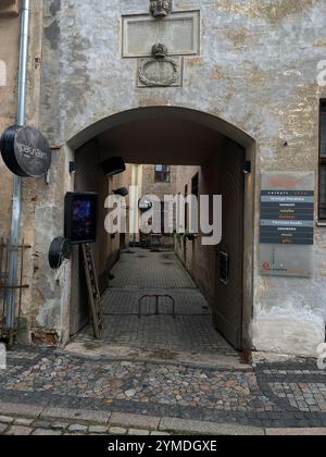 Eine enge Gasse mit einem Schild an der Wand, auf dem steht "Cafe". Die Gasse ist mit Kopfsteinpflaster gesäumt und hat einige Topfpflanzen. Lettland, Riga 08.10.2023 Stockfoto