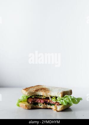 Ein Sandwich mit Salat und Fleisch wird in zwei Hälften geschnitten und auf einem weißen Hintergrund platziert. Das Sandwich ist halb gegessen, und der Biss wird daraus genommen Stockfoto