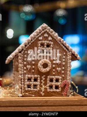 Ein hausgemachtes Lebkuchenhaus mit weißer Glasur und einem Zuckerrohr und winzigen Lichtern mit Bokeh-Hintergrund Stockfoto