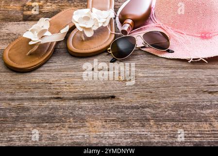 Strandzubehör. Sommerschuhe und Hut mit Sonnenbrille und Sonnencreme auf hölzernem Hintergrund Stockfoto