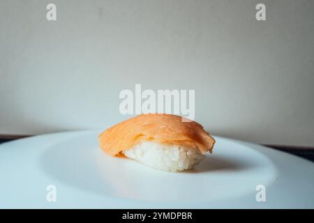 Ein Stück Sushi sitzt auf einem weißen Teller. Das Sushi ist orange und weiß und es ist das einzige Essen auf dem Teller Stockfoto