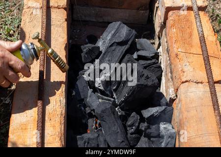 Ein Mann zündet Holzkohle in einem gemauerten Grill an, indem er einen Gaskanister mit einem Aufsatz benutzt. Stockfoto