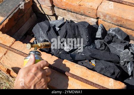 Ein Mann zündet Holzkohle in einem gemauerten Grill an, indem er einen Gaskanister mit einem Aufsatz benutzt. Stockfoto