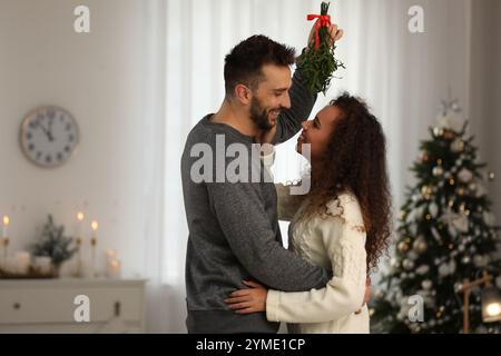 Ein reizendes Paar unter Mistelzweigen im Zimmer, das zu Weihnachten dekoriert war Stockfoto