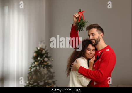 Ein reizendes Paar unter Mistelzweigen im Zimmer, das zu Weihnachten dekoriert war Stockfoto