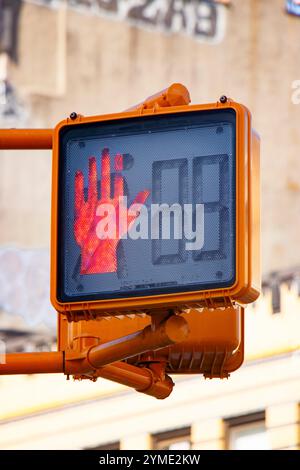 Städtisches Verkehrszeichen mit roter Hand, das den Stopp vor einer verschwommenen Kulisse des Stadtgebäudes anzeigt und die Fußgängersicherheit unterstreicht Stockfoto