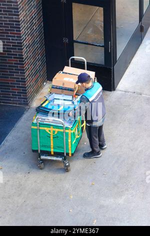 amazon Courier arrangiert Lieferpakete auf dem Bürgersteig des Einkaufswagens, neben dem Eingang eines Bürogebäudes im urbanen Ambiente manhattan New york Stockfoto