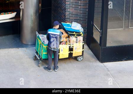 amazon Courier arrangiert Lieferpakete auf dem Bürgersteig des Einkaufswagens, neben dem Eingang eines Bürogebäudes im urbanen Ambiente manhattan New york Stockfoto