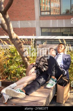Ein junges Paar gemischter Rassen umarmt sich auf einer stilvollen Holzbank im linearen Stadtpark Highline, im Grün von manhattan New york und in einer modernen Stadtlandschaft Stockfoto