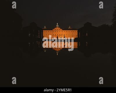 Ein großes Gebäude mit einem großen Fenster spiegelt sich im Wasser. Das Gebäude ist beleuchtet und schafft eine warme und einladende Atmosphäre Stockfoto