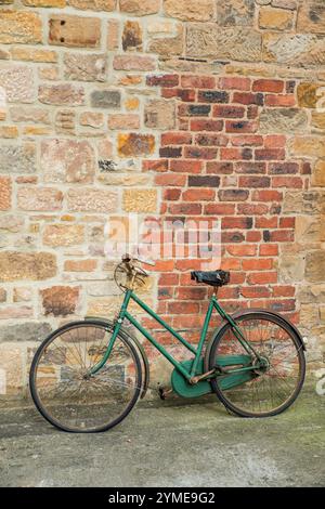 Ein grünes und rostiges, verlassenes Fahrrad, das sich an die Wand eines Gebäudes lehnt Stockfoto