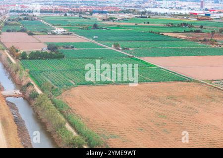 Luftaufnahme der landwirtschaftlichen Fläche mit mehreren rechteckigen Feldern mit Kulturen oder kürzlich gepflügten Feldern. Der Wasserkanal verläuft auf der linken Seite, umgeben von Schmutz Stockfoto