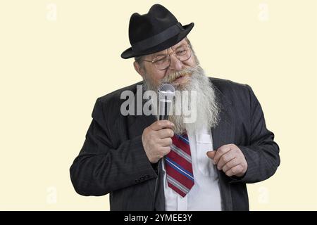 Porträt eines älteren langbärtigen Mannes mit Mikrofon. Isoliert auf pastellgelbem Hintergrund Stockfoto